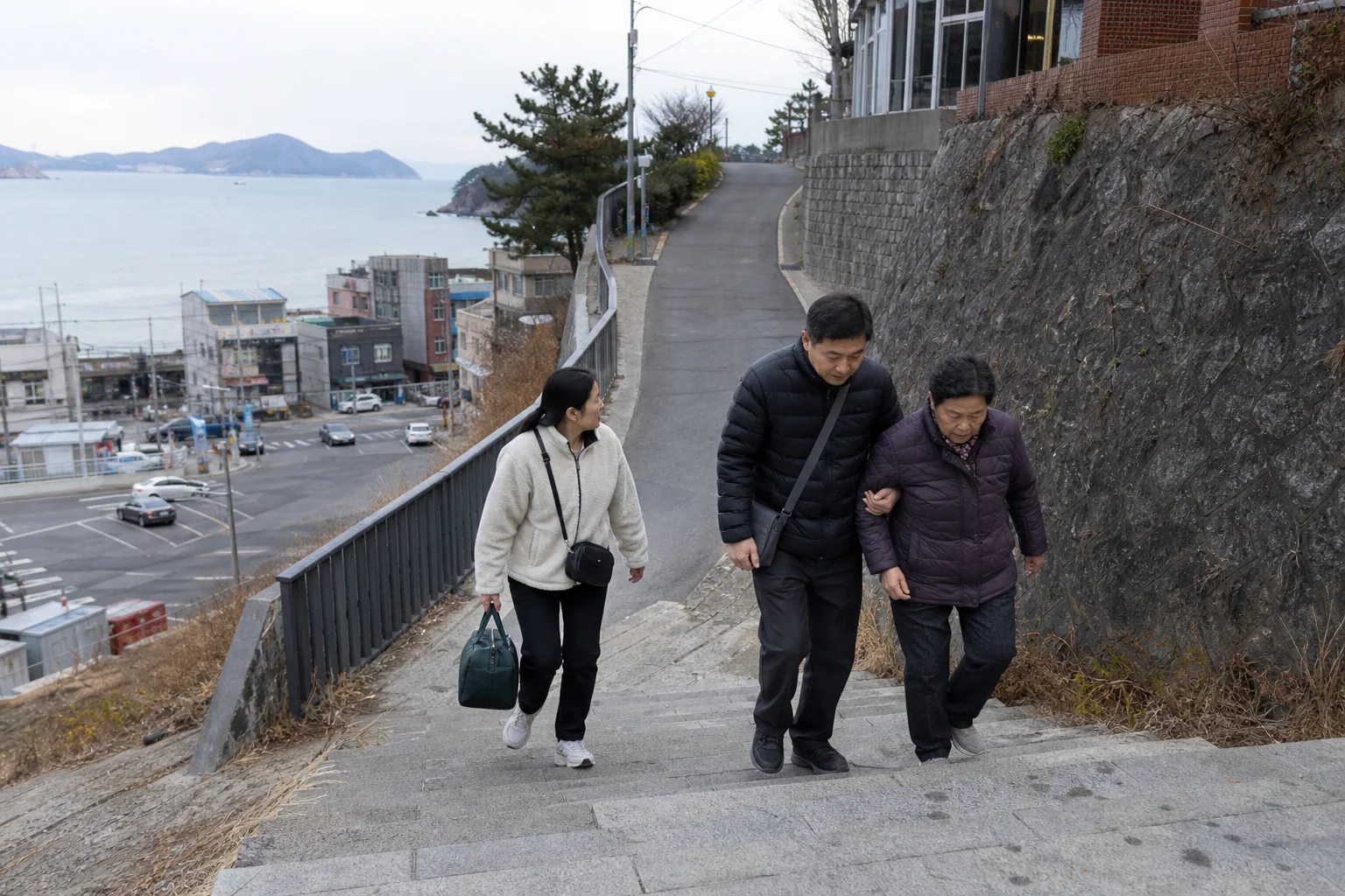바다와 해안 도로를 아래에 둔 세 사람이 작은 가방만 들고 어르신을 부축하며 마른 언덕길을 걸어 올라가는 상황 재구성 (AI 생성 삽화)